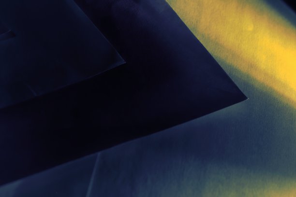 抽象的背景，由重叠的蓝色纸，创造几何图案，由一束黄色光横向照亮。图片下载