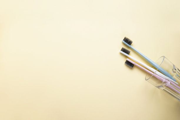 多色牙刷放在一个玻璃杯里，黄色的背景上有文字空间，平铺。图片下载