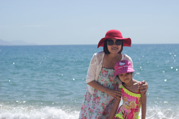 母亲和女儿在蓝色的大海，天空和建筑的海滩上微笑图片下载