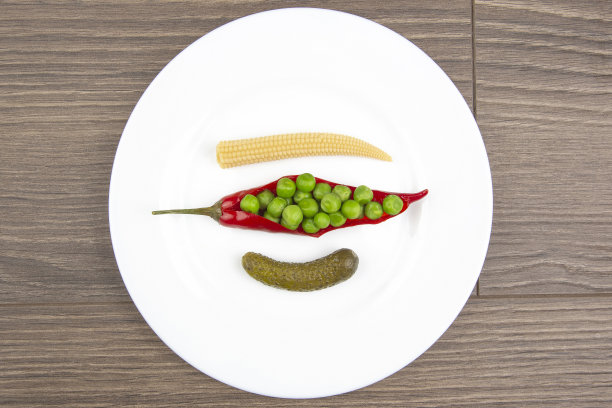 用白盘子盛着腌玉米、豌豆、黄瓜和红辣椒做成的沙拉。食物和蔬菜。饮食与减肥图片下载