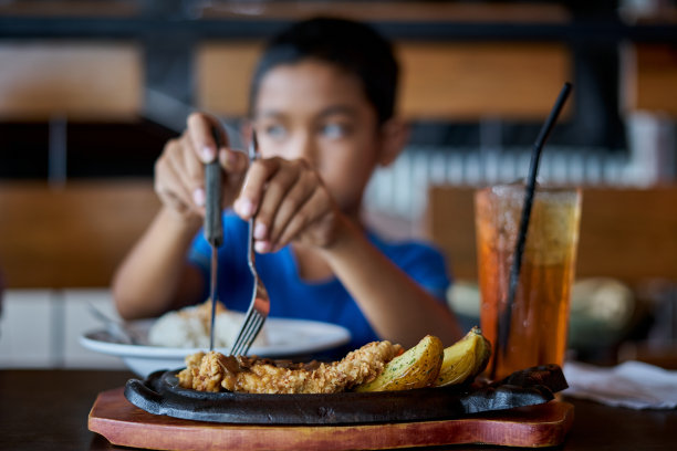 亚洲男孩拿着刀叉切烤鸡排在石头盘子在餐厅图片下载