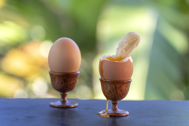 在自然背景的木桌上，蛋杯中的煮蛋和一片烤面包，特写图片下载