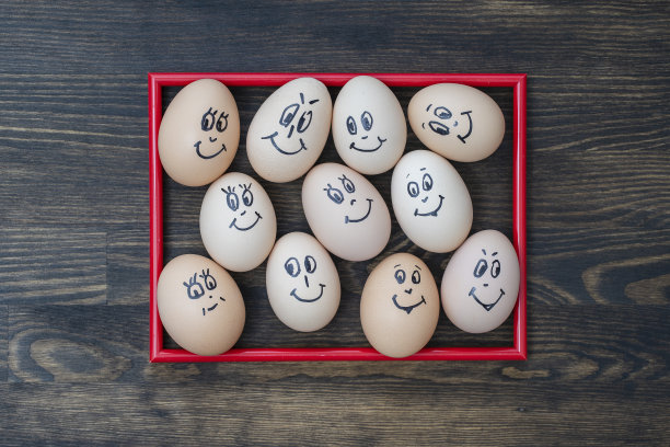 图片红框和许多有趣的鸡蛋微笑在木墙背景，特写。鸡蛋家庭情感面部肖像。概念有趣的食物图片下载