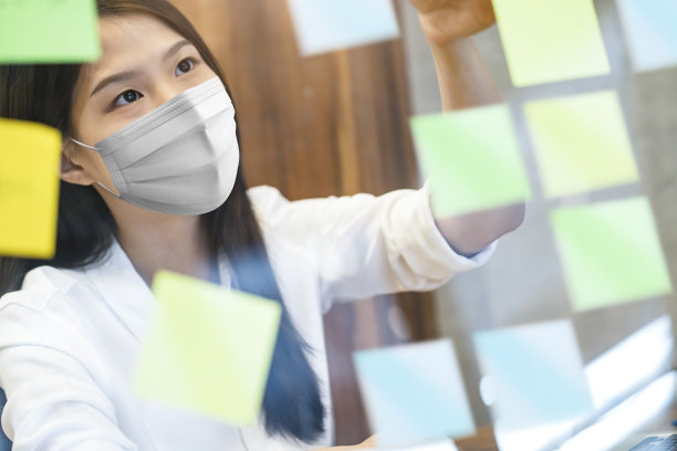 迷人的亚洲女性白衬衫工作，同时戴着防护病毒口罩在共同工作空间，有塑料隔断的社会距离座位新常态的生活方式素材图片