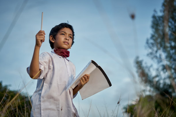 一个漂亮的男生拿着书和笔准备在自然公园学习的肖像图片下载