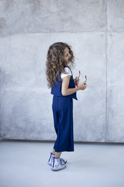 尺寸视图一个可爱的小女孩在蓝色制服和靴子，在红色眼镜，混凝土背景。回到学校的概念。图片下载