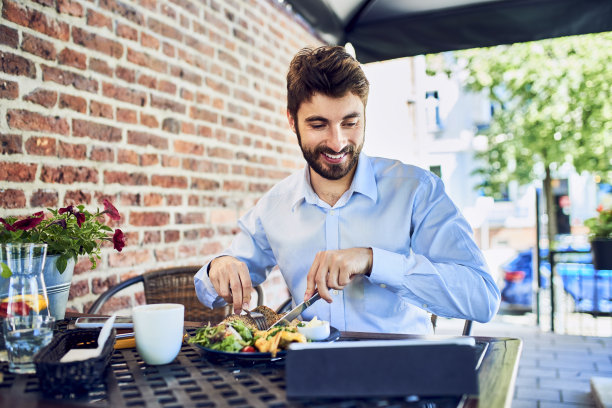这是一个年轻的商人在户外咖啡馆吃饭时看平板电脑的照片图片下载