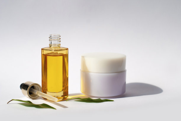 带有滴管的黄色玻璃。瓶子模型化妆油在白色背景与绿叶白色奶油。本空间图片下载