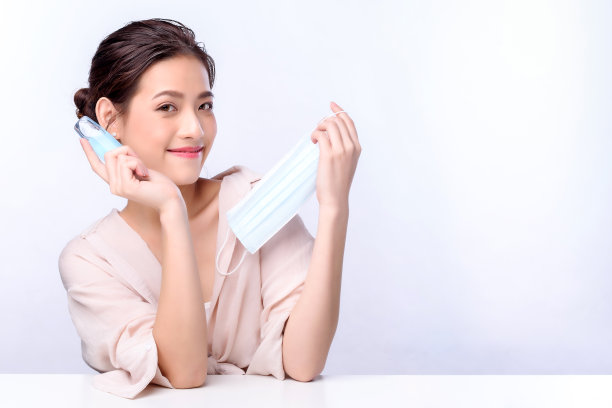 美丽迷人的亚洲年轻女性肖像，戴着外科口罩或面罩，以保护冠状病毒，坐在白色背景的白色桌子上，保护Covid-19健康素材图片
