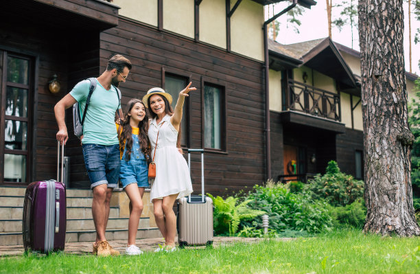 一个美丽的年轻游客家庭度假的照片，而他们站在森林酒店的背景和等待安顿在房间与背包和手提箱。图片下载