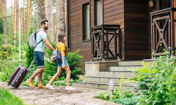 得到解决。照片中，一位父亲背着行李背着双肩包，牵着女儿的手来到了树木环绕的木质酒店。图片下载