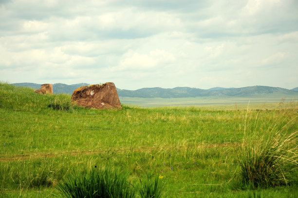 在无边无际的草原上，一个古老的坟堆的遗迹被高山环绕在背后。图片下载