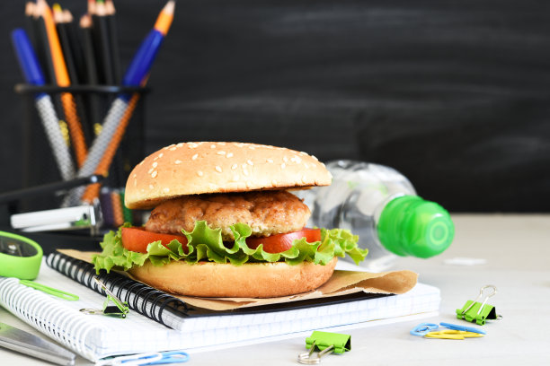 回到学校。隔离教育。午餐盒，汉堡，水和学校用品在学校董事会的背景。图片下载