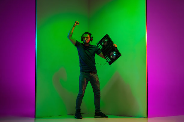 年轻的白人音乐家戴着耳机在霓虹灯下的绿紫双色背景上表演图片下载