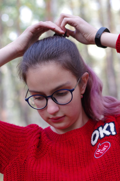 一个可爱的白人女孩的肖像戴着蓝色的眼镜，红色的毛衣，结的头发在森林里图片下载