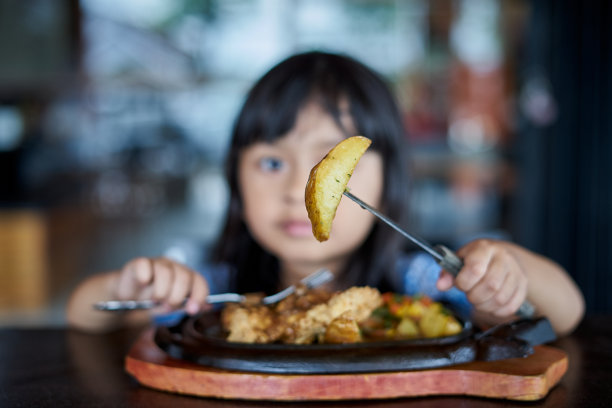 微笑的可爱的女孩吃牛排和展示一片油炸土豆图片下载