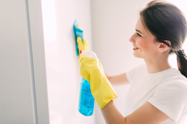 年轻微笑的妇女戴着黄色橡胶防护手套，用抹布和喷瓶清洁剂清洁冰箱。家,客房服务的概念。图片下载