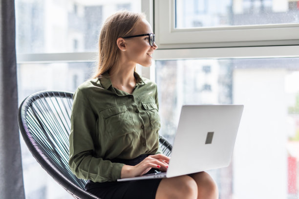 享受在家的时光。美丽的年轻女商人工作在笔记本电脑和喝咖啡，而坐在一个舒适的大椅子在家里图片下载