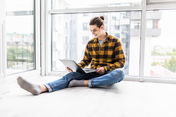 英俊的年轻人坐在地板上用笔记本电脑在家里图片下载