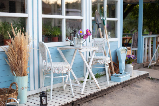 外立面蓝色舒适的家和一个美丽的花园在夏天。美丽的农舍与柳条篮子和绿色植物的梯田。房子阳台上的白色桌椅。院子里有园艺工具。图片下载
