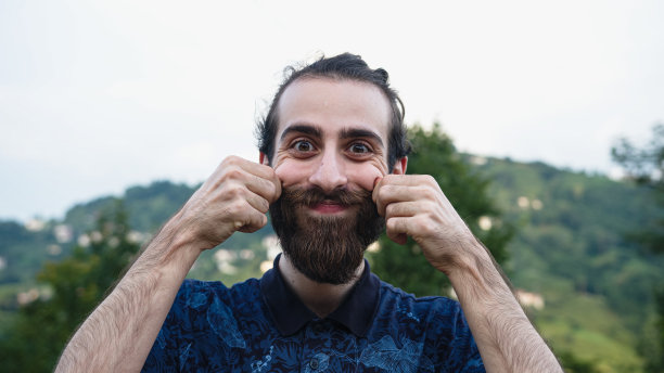 一个长发髻的嬉皮士看着镜头，摸着小胡子微笑着图片下载