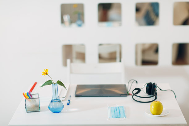 现代住宅内部工作空间，银色笔记本电脑，耳机，花瓶，花，苹果，口罩和笔在桌子上。图片下载