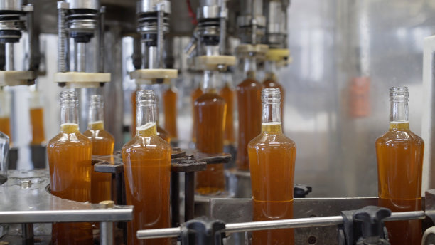 在酒精饮料装瓶工厂，玻璃瓶沿着输送线和灌装机的控制面板移动。梅子酊的生产工艺在现代化的工厂。图片下载