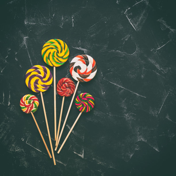 黑色石头背景上的条纹彩色漩涡棒棒糖。彩色糖果棒。俯视图，平铺，复制空间，色调。图片下载