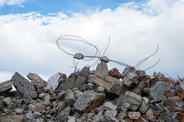 在蓝天和灰云的映衬下，一座被摧毁的建筑的混凝土碎片。背景图片下载