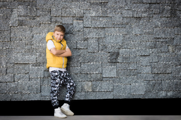 自信的孩子，双臂交叉倚靠在砖墙上。图片下载