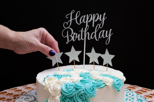 用白色和蓝色糖衣装饰的生日蛋糕。女人手上放着一颗点缀的星星。黑色背景。前视图。特写镜头图片下载