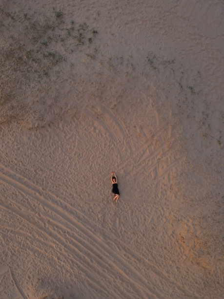 一个穿着黑色裙子的年轻女子躺在沙滩上。无人机俯视图。图片下载
