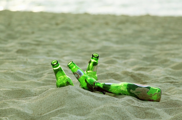 空的绿色玻璃瓶躺在沙滩上。图片下载