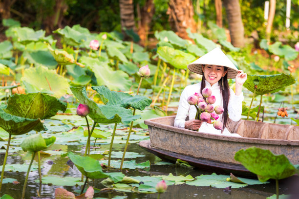一名越南亚洲妇女抱着莲花坐在木船上。图片下载