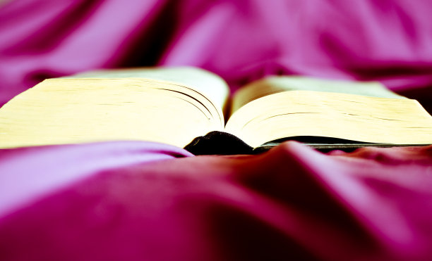 在紫色未整理的床上有一本打开的书图片下载
