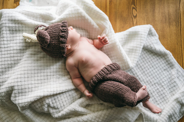 两个月大的新生儿穿着针织鹿装，微笑着躺在白色毯子上拍摄新生儿照片。精神运动发展和婴儿护理图片下载