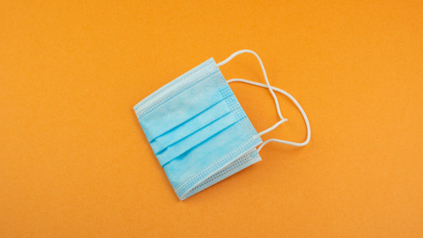 一次性医用防尘口罩，用于保护橙色背景的通勤者免受病毒和污染。个人防护用品由于全球流行的Covid - 19冠状病毒、污染。图片下载