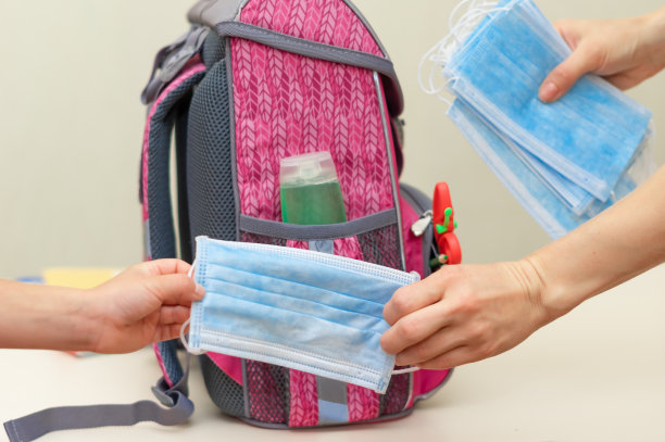回到学校。为上学收集一个背包。妈妈给孩子一个防护医用口罩。抗菌洗手液(洗手酒精)装于小背包内。教育的概念。社会距离。图片下载