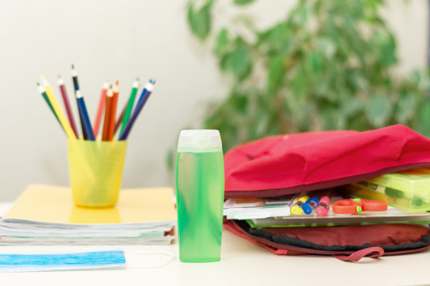 回到学校。教育和社会距离概念。红色背包旁边的桌子上放着医用防护口罩、抗菌洗手液(酒精凝胶)、学习用品。光背景。图片下载