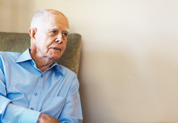 一名80多岁的男子坐在椅子上，望着一面空白的墙壁作为复印空间图片下载