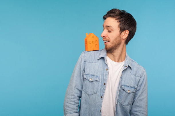 家购买。肖像快乐的人在牛仔衬衫看着微笑在他的肩膀上的纸房子图片下载
