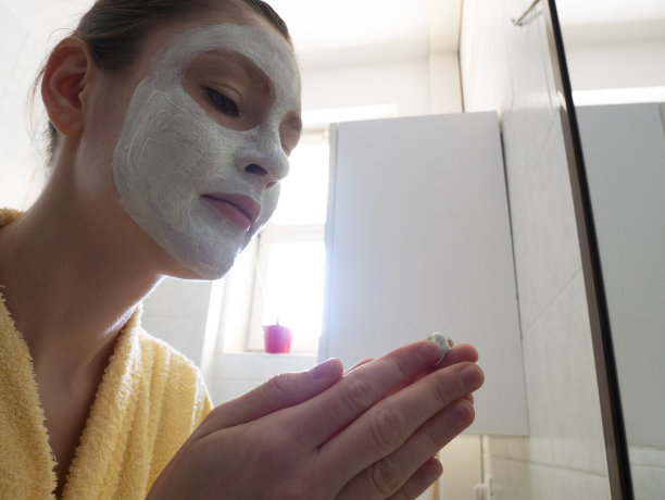 一名年轻女子在浴室的镜子前敷面膜。美容护理的概念。图片下载