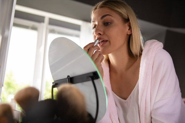 漂亮的年轻女子在镜子前涂口红图片下载