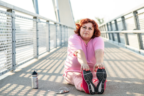 一个肥胖的女人正在一座桥上做体操，她旁边有一个手机和一瓶水图片下载
