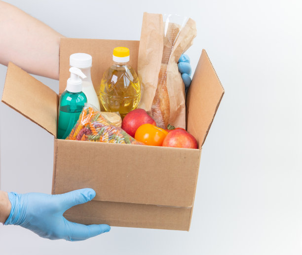 戴着乳胶手套的人拿着一个装有订购货物的箱子。被隔离的安全食品配送服务。网上食品购物服务或捐赠概念。白色背景。高质量的特写照片图片下载