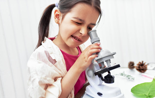 可爱的小女孩与显微镜和探索植物。穿着实验服的科学家小孩在学校的实验室里学习科学。孩子在看显微镜。图片下载