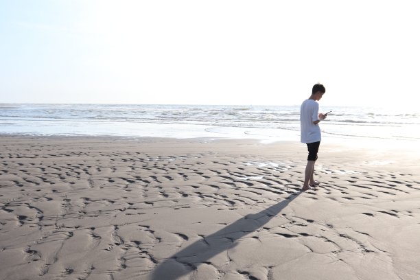 一名亚洲男子在海滩上用智能手机散步。图片下载