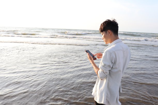 一名亚洲男子在海滩上用智能手机散步。图片下载