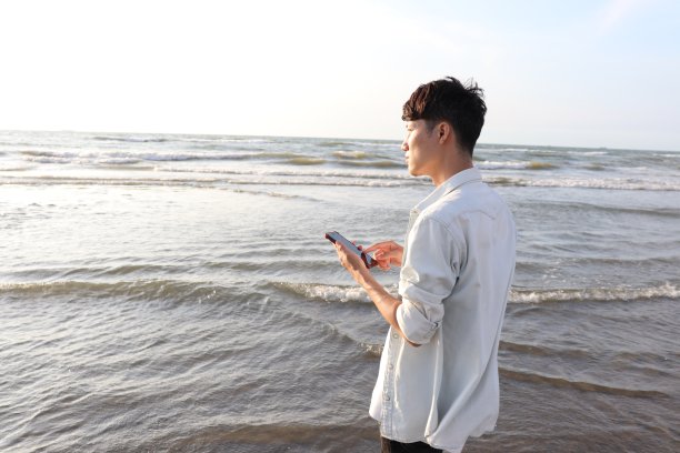 一名亚洲男子在海滩上用智能手机散步。图片下载