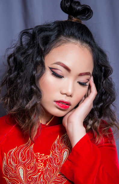 亚洲年轻女子特写，红色婚纱，与图形红色化妆，低头与闭上眼睛，在蓝色背景图片下载